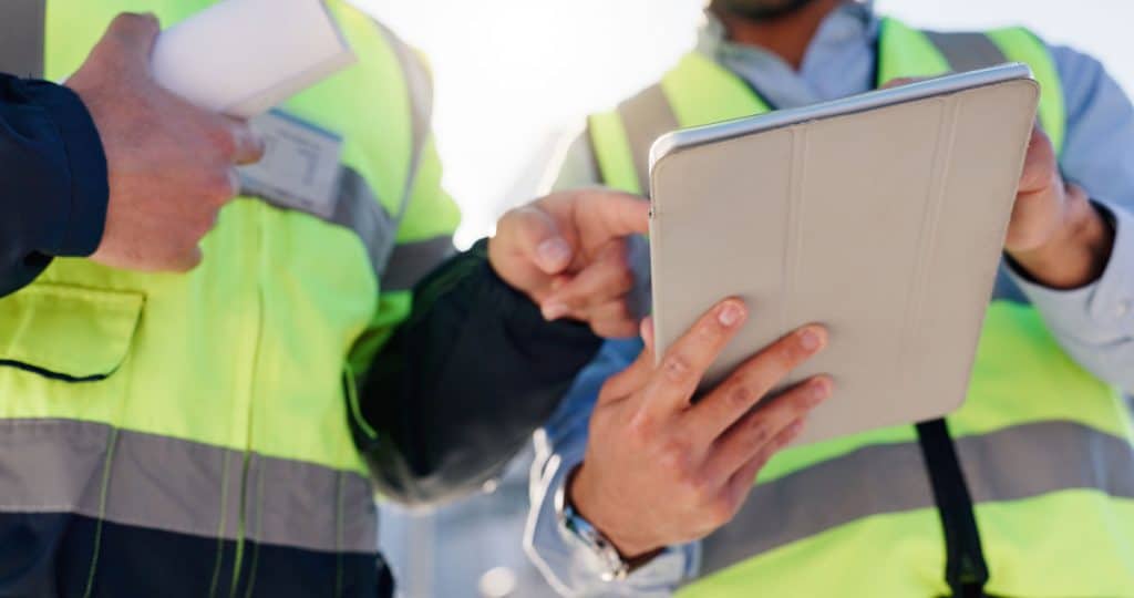 Workers in high viz consulting a tablet.