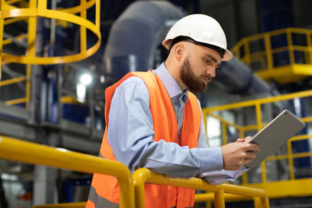 Man in a hard hat and hi viz vest making notes on a tablet