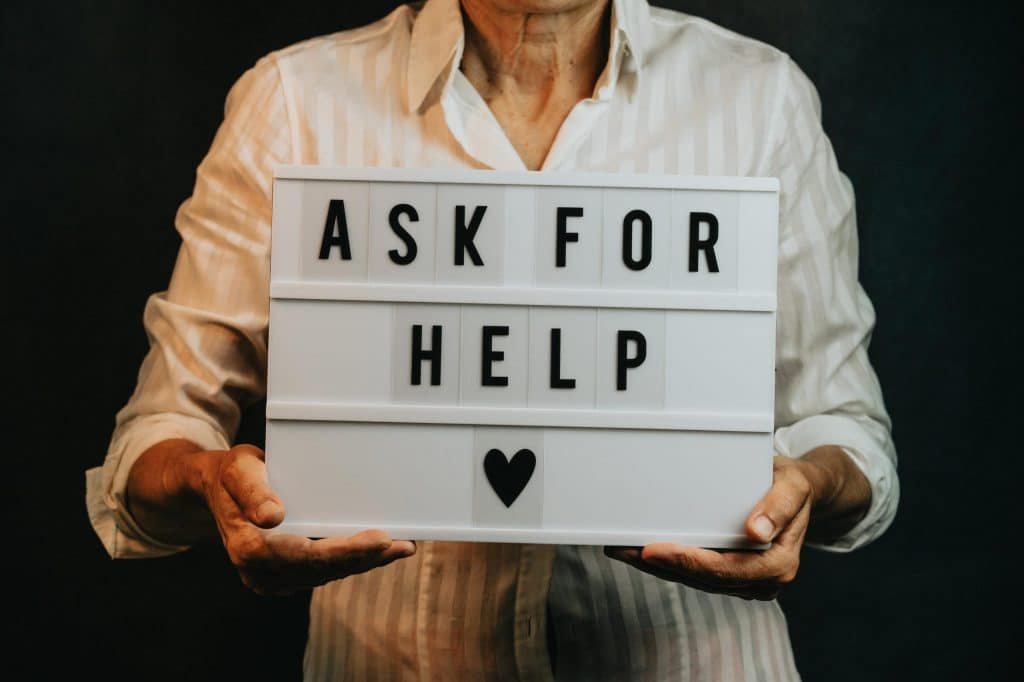 Person holding a sign that says "Ask for Help"